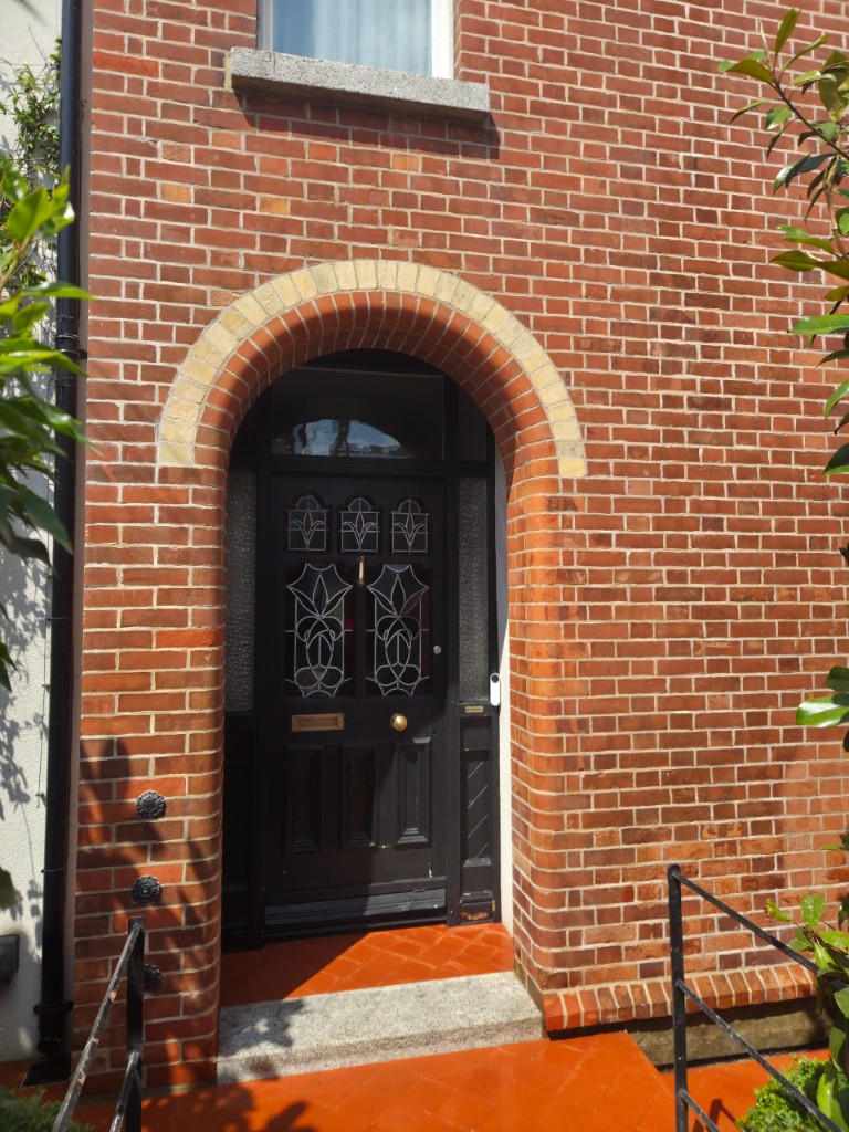 Repointed red brick arched doorway with black leaded-glass door in Dublin
